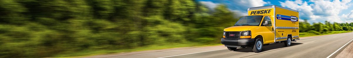 Penske 12 foot box truck driving on a tree-lined highway