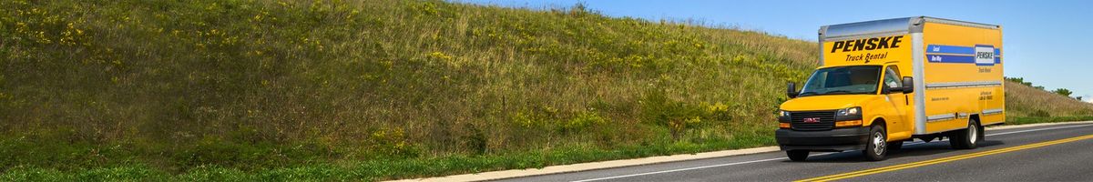 Penske 16 foot box truck driving on the highway by a field