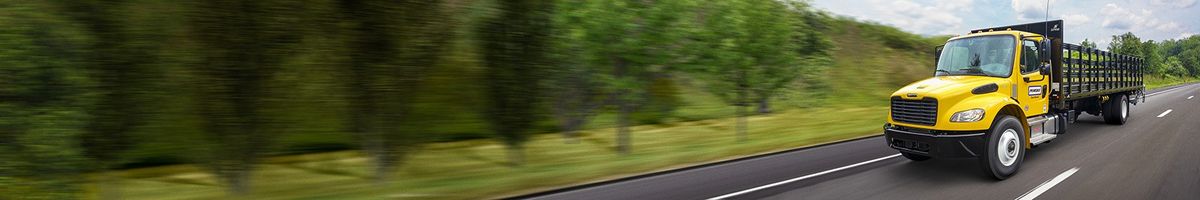 Penske flatbed truck driving on a tree-lined road