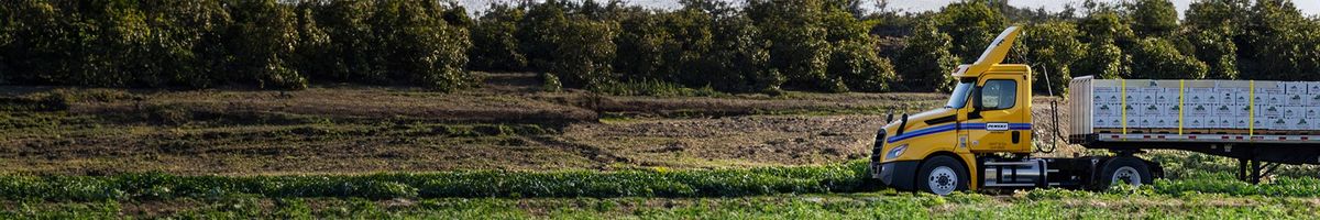 Penske single-axle day cab tractor driving through a green field