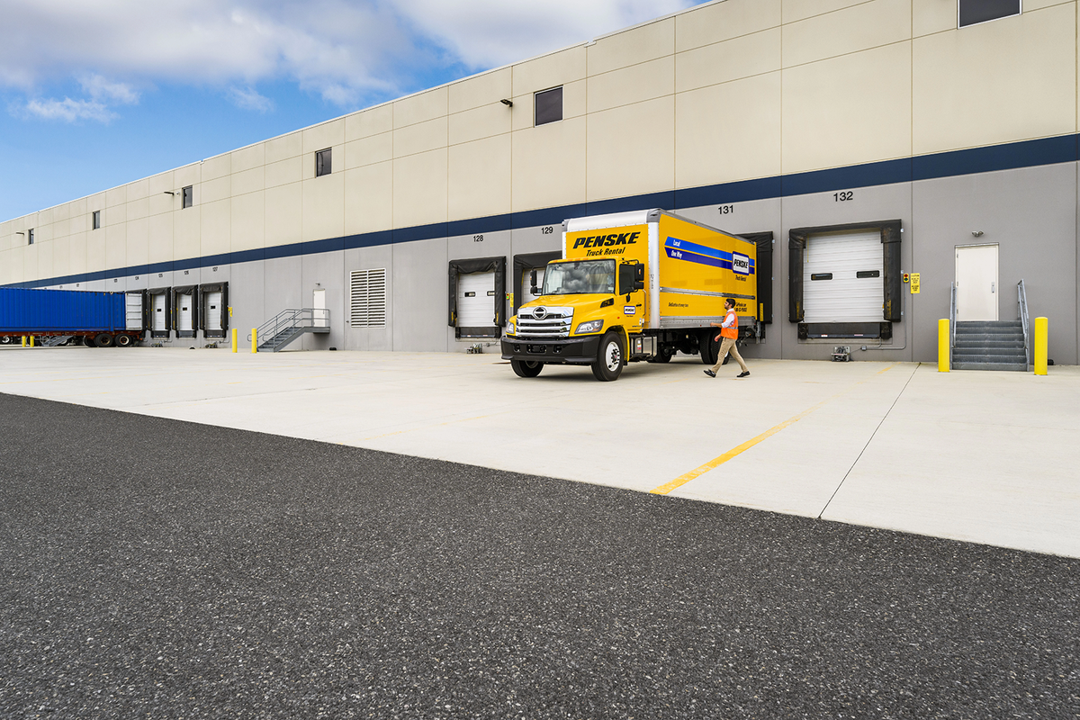 A person walks towards a yellow Penske truck parked at a loading dock.